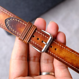 Pode incluir: Uma pulseira de rel&oacute;gio em couro castanho com acabamento degrad&ecirc; polido, costuras de contraste claras e uma fivela de metal prateado. A pulseira inclui dois passadores de couro e uma ponta, exibindo uma superf&iacute;cie texturizada.