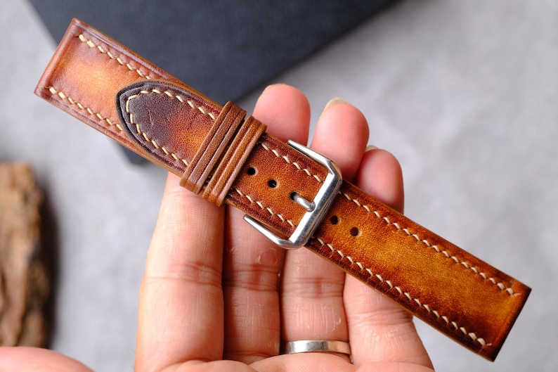 Pode incluir: Uma pulseira de rel&oacute;gio em couro castanho com acabamento degrad&ecirc; polido, costuras de contraste claras e uma fivela de metal prateado. A pulseira inclui dois passadores de couro e uma ponta, exibindo uma superf&iacute;cie texturizada.