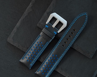 May include: A black leather watch strap featuring a perforated design with a vibrant blue underside and blue stitching. The strap includes a silver-toned metal buckle and two matching leather keepers, showcasing a textured surface finish.