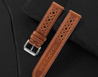 Könnte beinhalten: Ein hellbraunes Leder-Uhrenarmband mit perforiertem Design und mehreren kreisförmigen Ausstanzungen entlang der Mitte. Das Armband verfügt über eine polierte silberfarbene Metallschnalle und zwei passende Lederschlaufen mit sichtbaren Nähten.