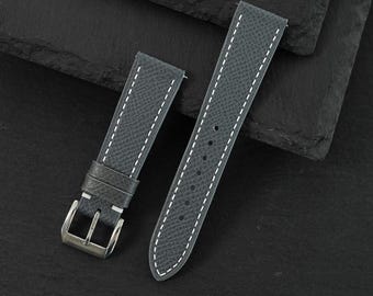 May include: A dark gray watch strap with a textured surface and white contrast stitching. The strap includes a silver-toned metal buckle and two sliding keepers on the shorter piece, while the longer piece features a series of punched holes.