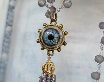 Artisan lampwork glass eye captured in brass pendant with resin, swings from knotted crystals necklace with crystal tassel