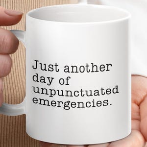 May include: White ceramic coffee mug with black text that reads "Just another day of unpunctuated emergencies."