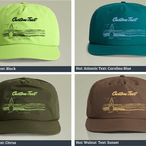 May include: Four different colored baseball caps with a surfboard graphic and the text "Custom Text" and "LOCATION". The caps are in the colors citrus, atlantic blue, army green, and walnut.