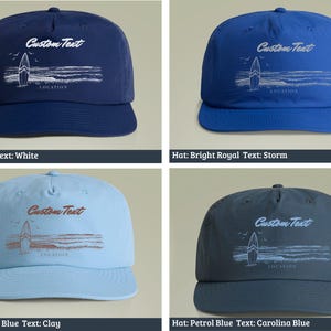 May include: Four different colored baseball caps with a white surfboard graphic and the text "Custom Text" in white. The caps are cobalt blue, bright royal blue, carolina blue, and petrol blue.