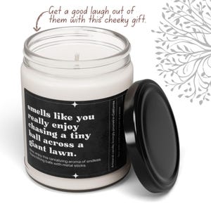 May include: A black and white candle with a humorous saying: "smells like you really enjoy chasing a tiny ball across a giant lawn." The candle is in a clear glass jar with a black lid.