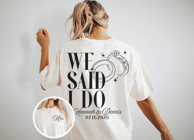 May include: Cream-colored t-shirt with the text "WE SAID I DO" in bold black letters, along with a graphic of two wedding rings and the names "Hannah & Dennis" and the date "07.16.2026".