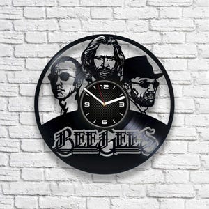May include: Black vinyl record clock featuring a silhouette of the Bee Gees band members. The clock face is a black and white grid pattern with white hands and numbers.