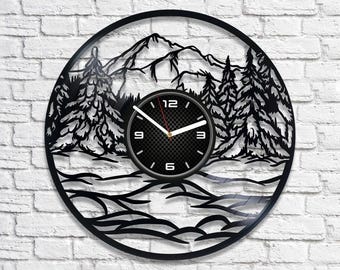 May include: Black vinyl record clock with a mountain and forest scene. The clock face has black numbers and hands.