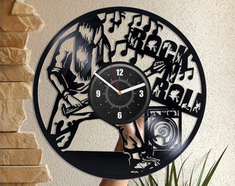 May include: Black vinyl record clock with a silhouette of a musician playing guitar and the words "Rock n Roll". The clock face is black with white numbers and hands.