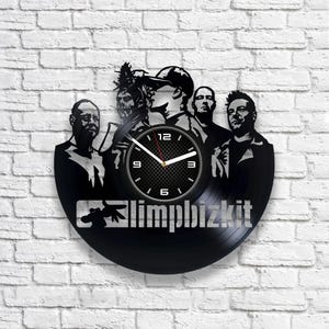 May include: Black vinyl record clock featuring a silhouette of the band Limp Bizkit. The clock face is white with black numbers and hands. The band members are silhouetted in black against a black background.
