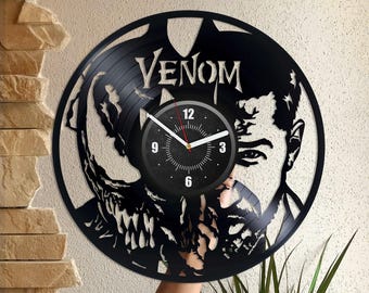 Könnte beinhalten: Schwarze Schallplattenuhr mit einer Silhouette von Venom aus dem Marvel Comics Universum. Das Zifferblatt der Uhr ist schwarz mit weißen Zahlen und Zeigern. Die Uhr ist mit "Venom" betitelt.