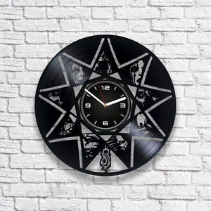 May include: Black vinyl record clock featuring a star design with the band Slipknot's logo and band members' faces. The clock face has a black and gray carbon fiber design with white numbers and hands.