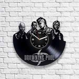Op de afbeelding: Zwarte vinyl platen klok met een silhouet van de band Drowning Pool. De wijzerplaat van de klok is wit met zwarte cijfers en wijzers. Het logo van de band is zichtbaar onder de wijzerplaat.