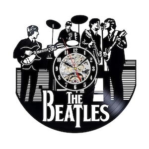 May include: Black and white wall clock featuring a silhouette of The Beatles band members. The clock face is visible, with the band's name at the bottom. The clock hands are red and gold.