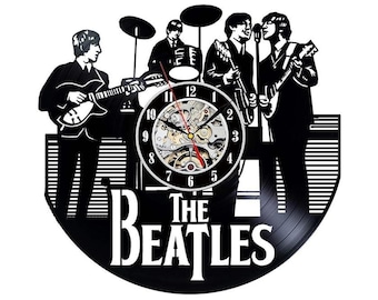 May include: Black and white wall clock featuring a silhouette of The Beatles band members. The clock face is visible, with the band's name at the bottom. The clock hands are red and gold.