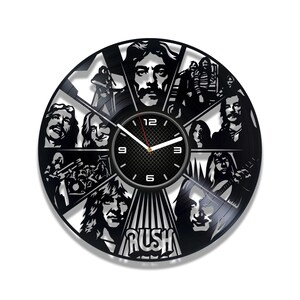 May include: A black vinyl record clock featuring the band Rush. The clock face is a black and white image of the band members, with the band's name "Rush" in white letters at the bottom. The clock hands are black and white.