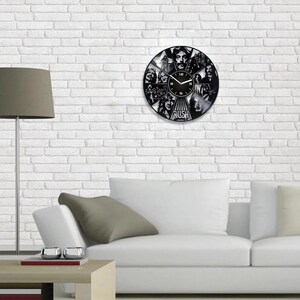 May include: A black vinyl record clock featuring a band's logo and band members' faces. The clock has a black background with white numbers and hands. The band's name "RUSH" is printed in white at the bottom of the clock.