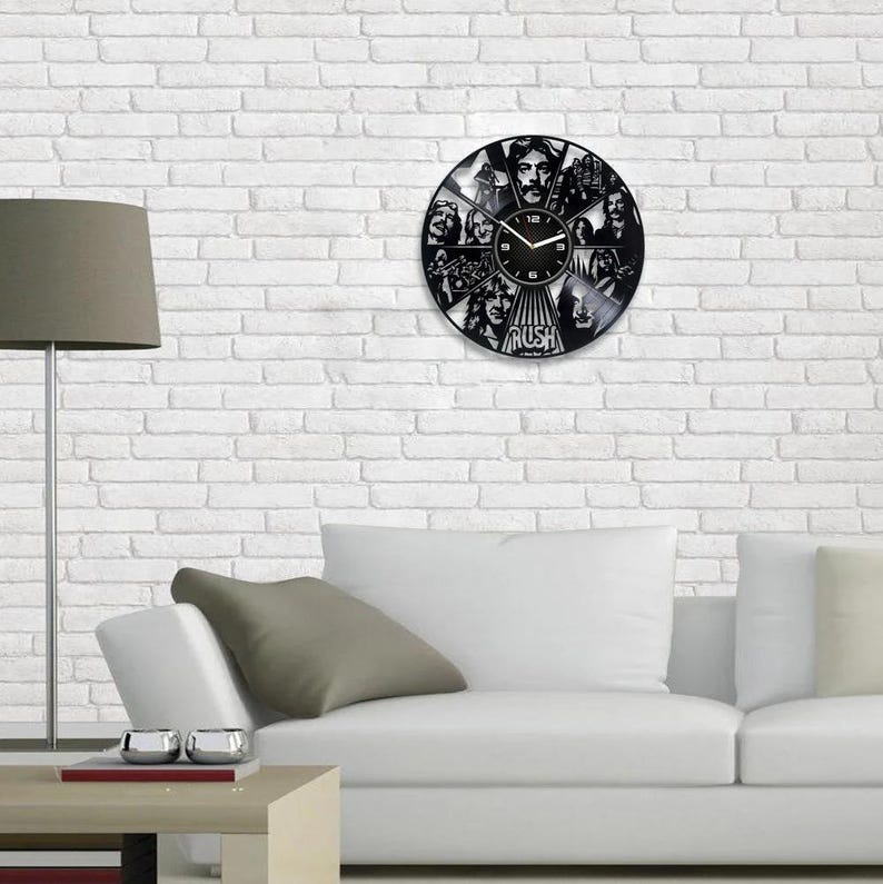 May include: A black vinyl record clock featuring a band's logo and band members' faces. The clock has a black background with white numbers and hands. The band's name "RUSH" is printed in white at the bottom of the clock.