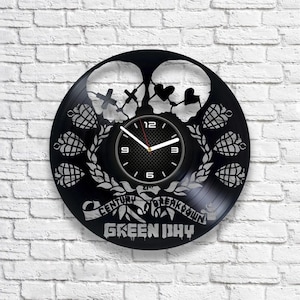May include: Black vinyl record clock featuring a Green Day logo with the band's name and "Century Breakdown" text. The clock face is a black and white design with a clock face and hands.