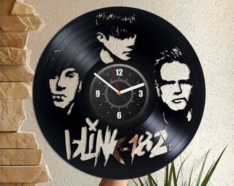 Könnte beinhalten: Schwarze Schallplattenuhr mit dem Band Blink-182. Das Zifferblatt der Uhr ist weiß mit schwarzen Zahlen und Zeigern. Der Name der Band ist in Weiß auf der Schallplatte geschrieben.