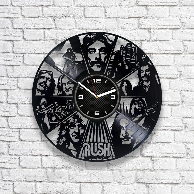 May include: Black vinyl record clock featuring a silhouette of the band Rush. The clock face is black with white numbers and hands. The band's name is printed in white at the bottom of the clock.