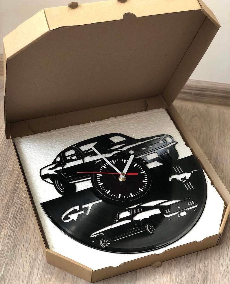 May include: A black vinyl record clock featuring a silhouette of a Ford Mustang GT. The clock face is black with white hands and numbers. The record is mounted on a white foam board inside a brown cardboard box.