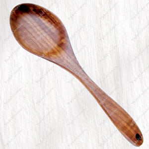 May include: A large wooden serving spoon with a smooth, polished finish. The spoon is a warm brown colour and has a hole in the handle. Text on the left side reads "Large Serving Spoon CNC File" with file type options and "Instant Download".