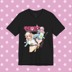 Può includere: Una t-shirt nera a maniche corte con una stampa grafica di due personaggi anime con capelli rosa, cuffie e una chitarra. Il design include testo giapponese e le parole SUPER SONICO THE ANIMATION in una combinazione di colori bianco e rosa.
