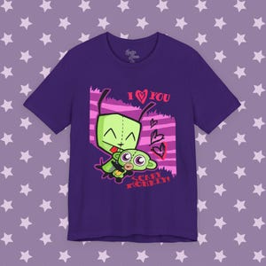 May include: A dark purple short-sleeve t-shirt featuring a graphic of a green alien character holding a green monkey toy. The text reads I LOVE YOU and SCARY MONKEY in red and pink, accompanied by heart illustrations against a pink striped background.