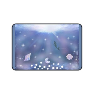 Könnte beinhalten: Eine rechteckige Schreibtischunterlage mit einer Unterwasserszene auf einem dunkelblauen und violetten Hintergrund. Das Design zeigt die Silhouette einer Meerjungfrau, drei helle Muscheln sowie zahlreiche leuchtende weiße Kreise und Sterne.