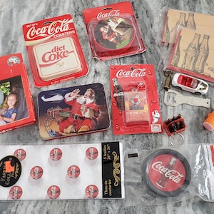 May include: A collection of Coca-Cola branded items, including coasters, a keychain with miniature bottles, a bottle opener, and a toy car. The items feature the Coca-Cola logo and vintage designs.