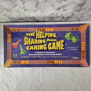 May include: A rectangular board game box titled The Helping, Sharing and Caring Game. The purple box features yellow text, green dice, orange and green game pawns, and illustrations of colourful hands and human figures along the borders.