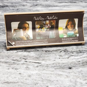 May include: A light-colored wooden photo frame with a dark brown insert. The insert has the words "PhotoFrame - Photo Cadre" and instructions for removing paper. The frame has a curved design and holds multiple photos.