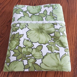 May include: Folded green and white floral patterned sheet set with a white lace trim. The sheets feature large, stylized green flowers and leaves against a white background. The set is neatly folded, showcasing the design.