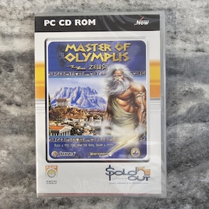 May include: A PC CD-ROM game case for Master of Olympus Zeus. The cover features a bearded figure, a mountain landscape, and ancient architecture. Text includes Master of Olympus Zeus, Build a City, Challenge the Gods, Spawn a Myth, Sierra, Impressions Games, and Sold Out Software.