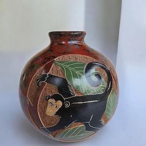 May include: A white ceramic mug with a black handle and the text "But First, Coffee" in a bold, black font. The mug is set against a blurred background, suggesting a cozy setting.