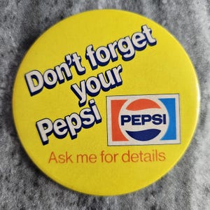 May include: A round, yellow Pepsi button with the text "Don't forget your Pepsi" in white and blue. The Pepsi logo is in the lower right corner, with the text "Ask me for details" below.