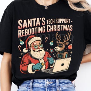 May include: Black t-shirt featuring a graphic of Santa Claus in a red suit and hat, fixing a laptop with a screwdriver. The text reads "SANTA'S TECH SUPPORT - REBOOTING CHRISTMAS". A reindeer with a computer screen is also in the graphic.