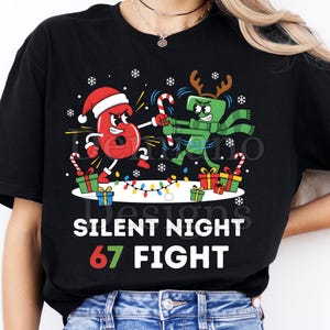 May include: Black t-shirt with a Christmas graphic. The design shows the numbers "6" and "7" as cartoon characters, with the text "SILENT NIGHT 67 FIGHT". The "6" wears a Santa hat, and the "7" has antlers. Festive and fun.