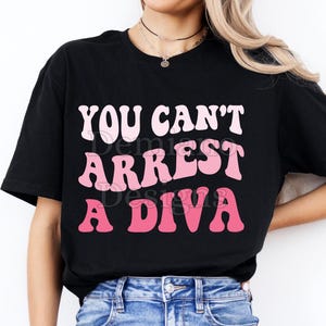 Puede incluir: Camiseta negra con el texto "YOU CAN'T ARREST A DIVA" en letras blancas y rosas. El diseño está disponible como archivo digital en formatos SVG y PNG. La imagen también incluye el texto "300DPI/ SVG + PNG/DIGITAL FILE".