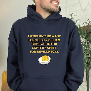 Può includere: Felpa con cappuccio blu navy con la scritta gialla "I WOULDN'T DO A LOT FOR TURKEY OR HAM BUT I WOULD DO SKETCHY STUFF FOR DEVILED EGGS". Presenta una grafica di uova alla diavola.