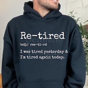 Puede incluir: Una sudadera con capucha azul marino con la palabra "Re-tired" en blanco, junto con una definición y la frase "I was tired yesterday & I'm tired again today." La parte inferior de la imagen dice "300DPI/ SVG + PNG/DIGITAL FILE."