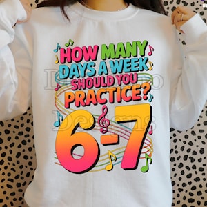 Op de afbeelding: Witte sweatshirt met een kleurrijke afbeelding. De afbeelding toont de vraag "HOW MANY DAYS A WEEK SHOULD YOU PRACTICE?" met de cijfers "6-7" in een oranje-rode gradiënt. Muzieknoten en krullen omringen de tekst.