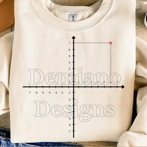 May include: Cream-colored sweatshirt featuring a coordinate plane graphic with the text "Demiano Designs." The design includes a pink 'x' at the point (6,7). The bottom of the image reads "300DPI / SVG+PNG / DEGITAL FILE."