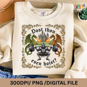 May include: Cream-colored sweatshirt featuring a medieval-themed graphic. The design includes a knight lifting weights, flanked by green and brown dragons, with a castle in the background. The text "Dost thou even hoist?" is also included.
