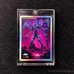 May include: A Victor Wembanyama The Alien Alter Egos trading card encased in a clear magnetic plastic holder. The card features a multi-armed figure against a vibrant pink and purple background with a city skyline and the Topps Chrome logo.