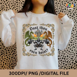 May include: White sweatshirt with a medieval-themed graphic. The design features a knight lifting weights, flanked by green and brown dragons breathing fire, with a castle in the background. Text reads "Dost thou even hoist?" at the top and bottom.