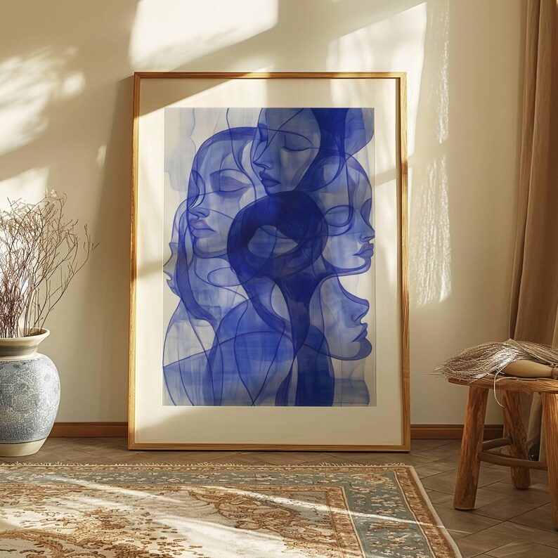 a large framed artwork depicting abstract blue and white human faces, placed on a wooden floor in a room with a rug and a vase.