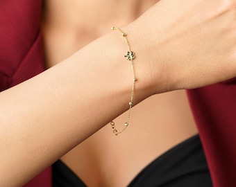 May include: A delicate gold bracelet featuring a four-leaf clover charm and small beaded accents. The bracelet is displayed on a wrist, showcasing its elegant design. The jewelry is a stylish accessory.